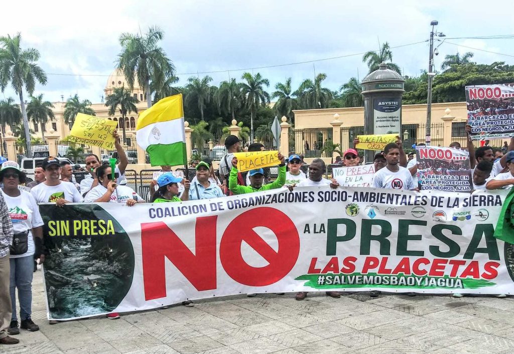 Santo Domingo, DN. - En una manifestación sin precedentes, cientos de serranos se congregaron frente al Palacio Nacional para manifestar su rechazo al proyecto de construcción de la presa de Las Placetas, exigiendo al presidente Luis Abinader que desista de su realización. Esta iniciativa, de llevarse a cabo, tendría consecuencias desastrosas, ya que secaría los ríos Jagua y Bao, fuentes vitales de agua en la región. Los serranos, organizados en la Coalición Socioambiental en defensa de La Sierra y respaldados por la Red Socioambiental Nacional, la Coordinadora Popular Nacional y otras organizaciones de diferentes puntos del país, denunciaron enérgicamente los daños al medio ambiente que ocurren ante la mirada indiferente de las autoridades, y en muchos casos, con la complicidad del Ministerio de Medio Ambiente. Durante la concentración, los manifestantes leyeron un manifiesto que le se exige al gobierno la cancelación del proyecto de la presa de Las Placetas, así como de otras obras que están generando una calamidad ambiental en el país y que desista del intento de privatizar el agua. El llamado se hizo de forma oportuna, previo al Día Internacional del Medio Ambiente, que se celebra este lunes 5 de junio. La presa de Las Placetas ha generado un gran rechazo desde su anuncio inicial en el 2007. Los opositores al proyecto argumentan que la construcción de la presa provocaría la desaparición de los ríos Jagua y Bao, lo que tendría un impacto devastador en el ecosistema local y en las comunidades que dependen de estas fuentes de agua. “Emplazamos al presidente Luis Abinader, al conjunto del Gobierno y la élite financiera y empresarial a que en el curso de este mes de junio respondan las demandas y propuestas de las comunidades y sectores movilizados por sus derechos hoy desplegados aquí frente al Palacio Nacional”. Dijo Llaniris Espinal activista de la Coalición Socioambiental de La Sierra y la Fundación Ecológica Tropical (FUNDETROP). La manifestación también contó con la presencia de destacadas figuras del activismo medioambiental nacional, quienes expresaron su apoyo a los serranos y resaltaron la urgencia de tomar medidas concretas para evitar la destrucción de los recursos naturales del país. Hasta el momento, el gobierno no ha emitido una respuesta oficial ante las demandas de los manifestantes. Sin embargo, la presión ejercida por los serranos y las organizaciones ambientales ha generado un intenso debate público sobre la necesidad de proteger el medio ambiente y tomar decisiones responsables en relación con el desarrollo de proyectos que afecten los recursos naturales. La lucha de los serranos contra la presa de Las Placetas se empodera aun más llegando hasta el Palacio Nacional, recordando a todos la importancia de preservar los ríos Jagua y Bao, y proteger el entorno natural para las generaciones presentes y futuras.